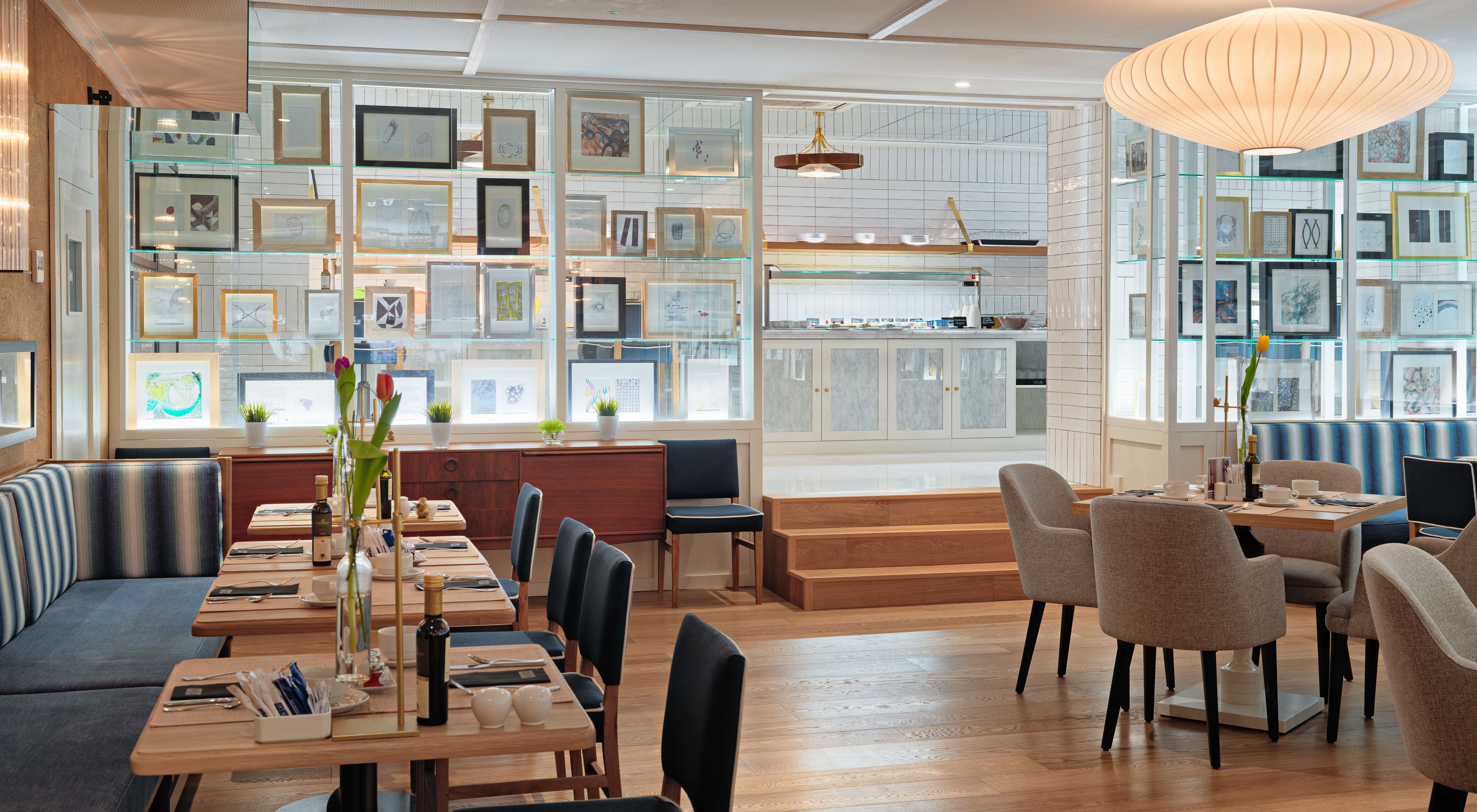Un comedor moderno con una larga mesa de madera, asientos acolchados y vistas a una cocina con encimera de mármol.