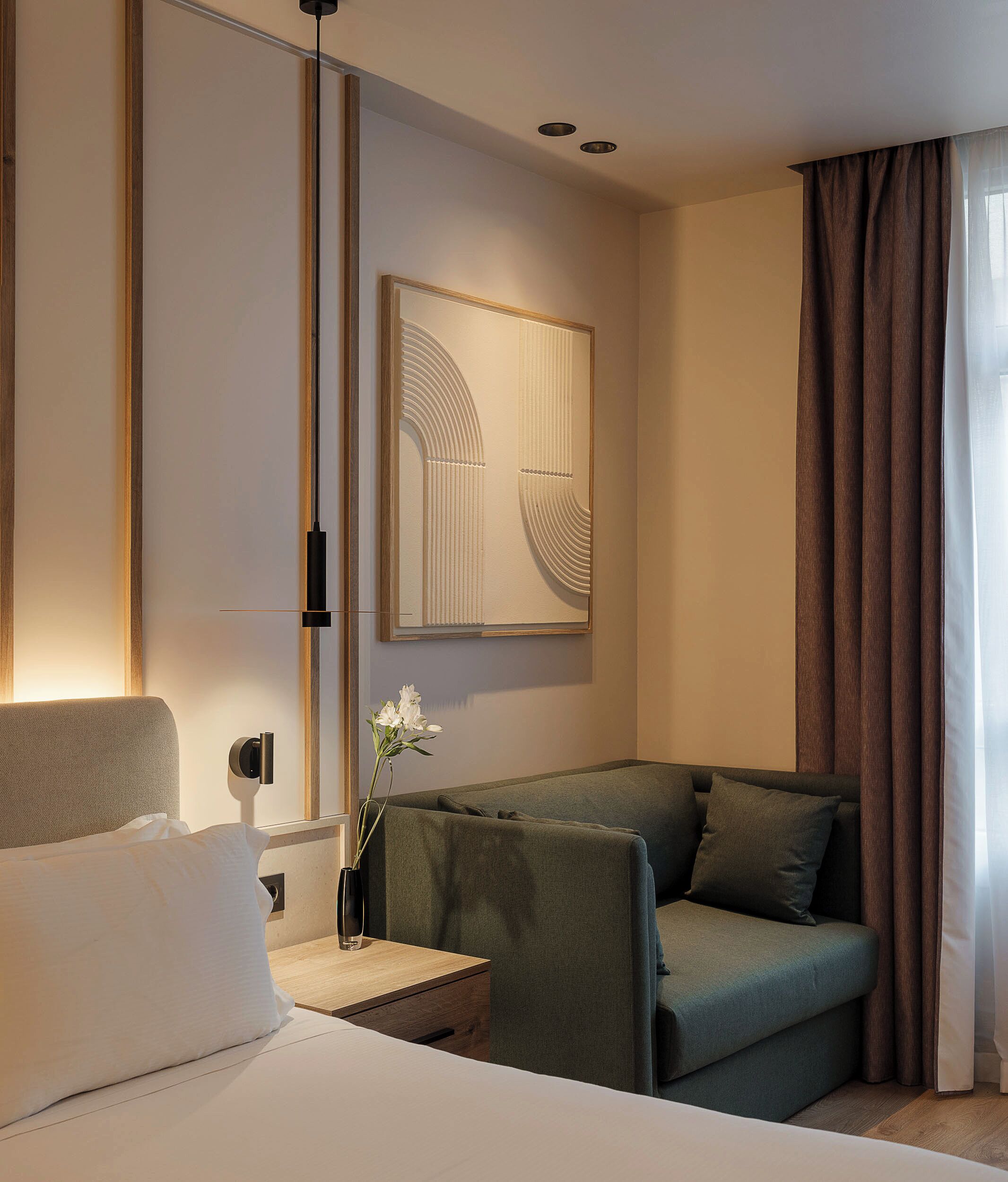 Ein modernes Hotelzimmer mit Bett, einer Couch, einem Nachttisch mit Blumenvase und einem großen, abstrakten Kunstwerk an der Wand.