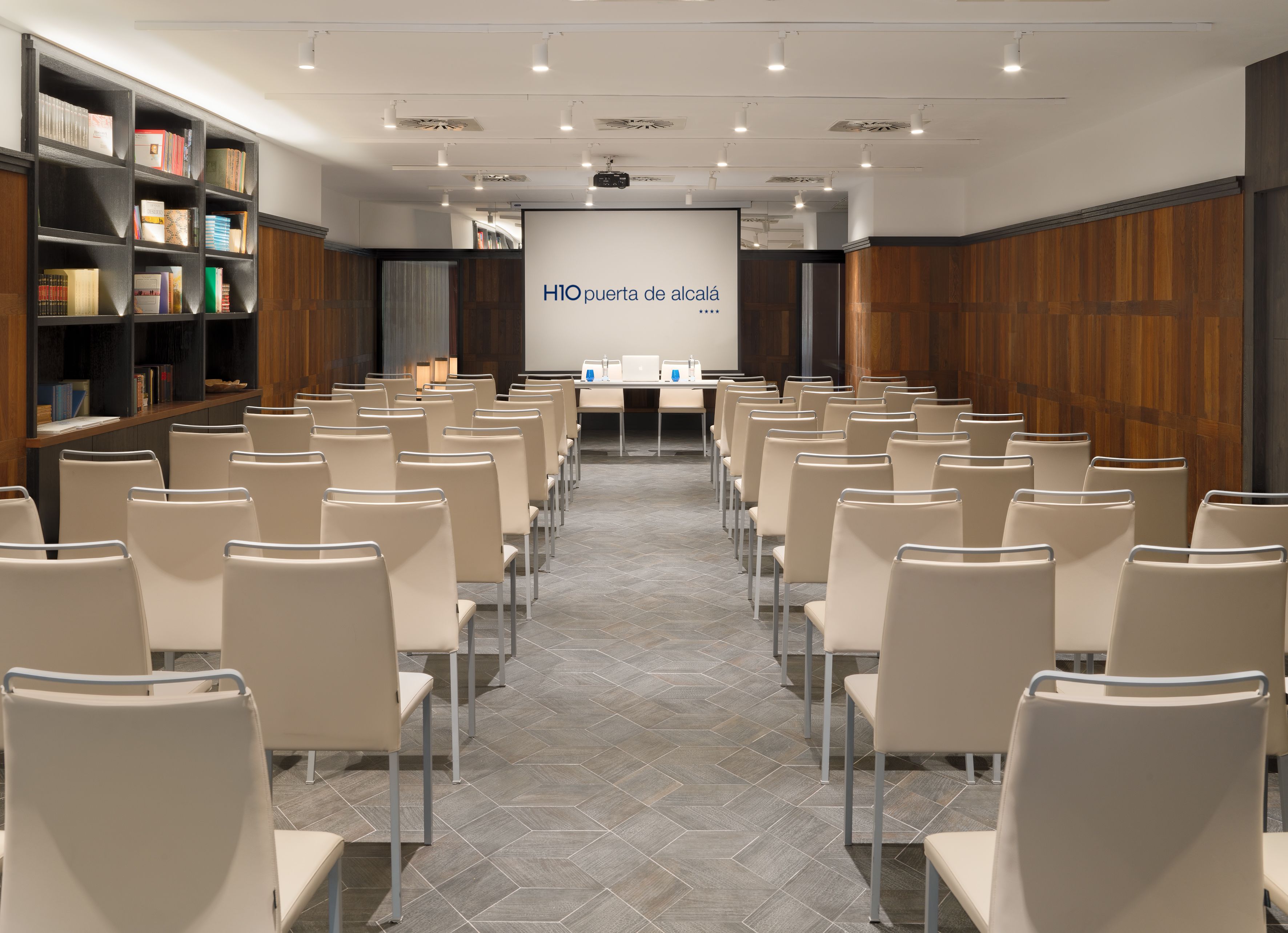 A conference room with rows of chairs, a projector screen, and a bookshelf with books.
