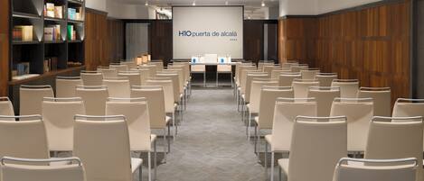 A conference room with rows of chairs, a projector screen, and a bookshelf with books.