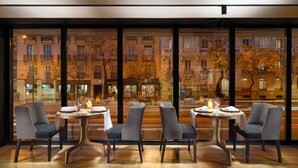 A restaurant with a view of a cityscape at night, featuring tables set with wine glasses and plates, and modern chairs. - H10 Puerta de Alcalá 4* Sup (Madrid)