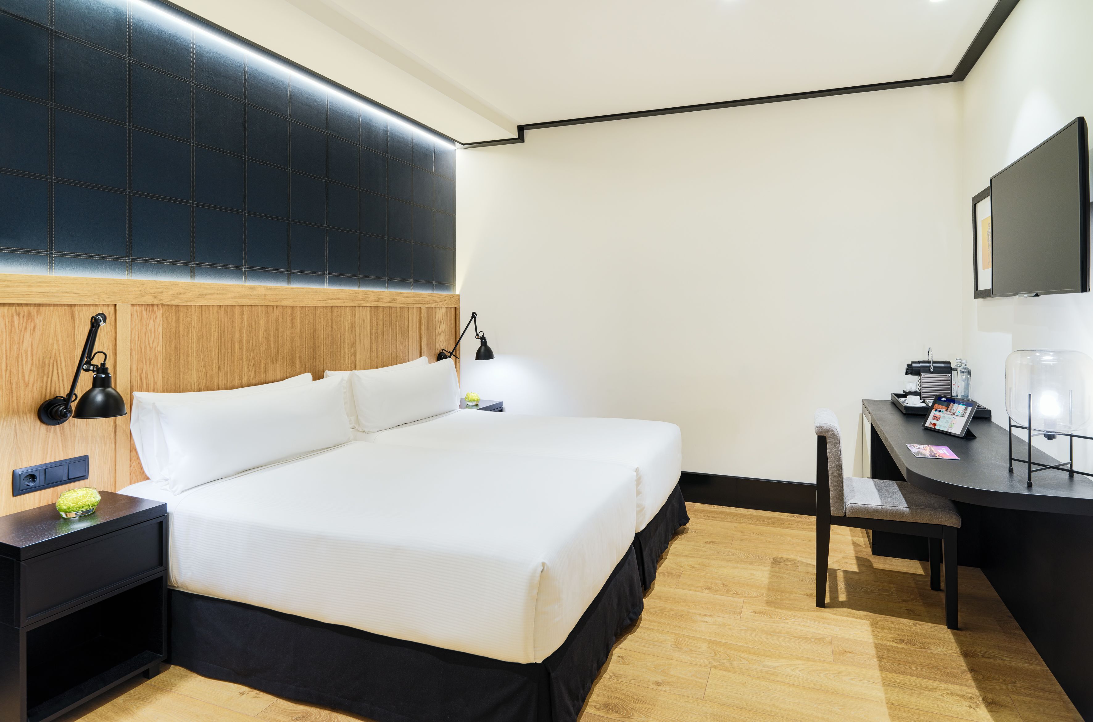 Een hotelkamer met een groot bed, nachtkastjes, een bureau met stoel, een flatscreen televisie en een houten hoofdbord.