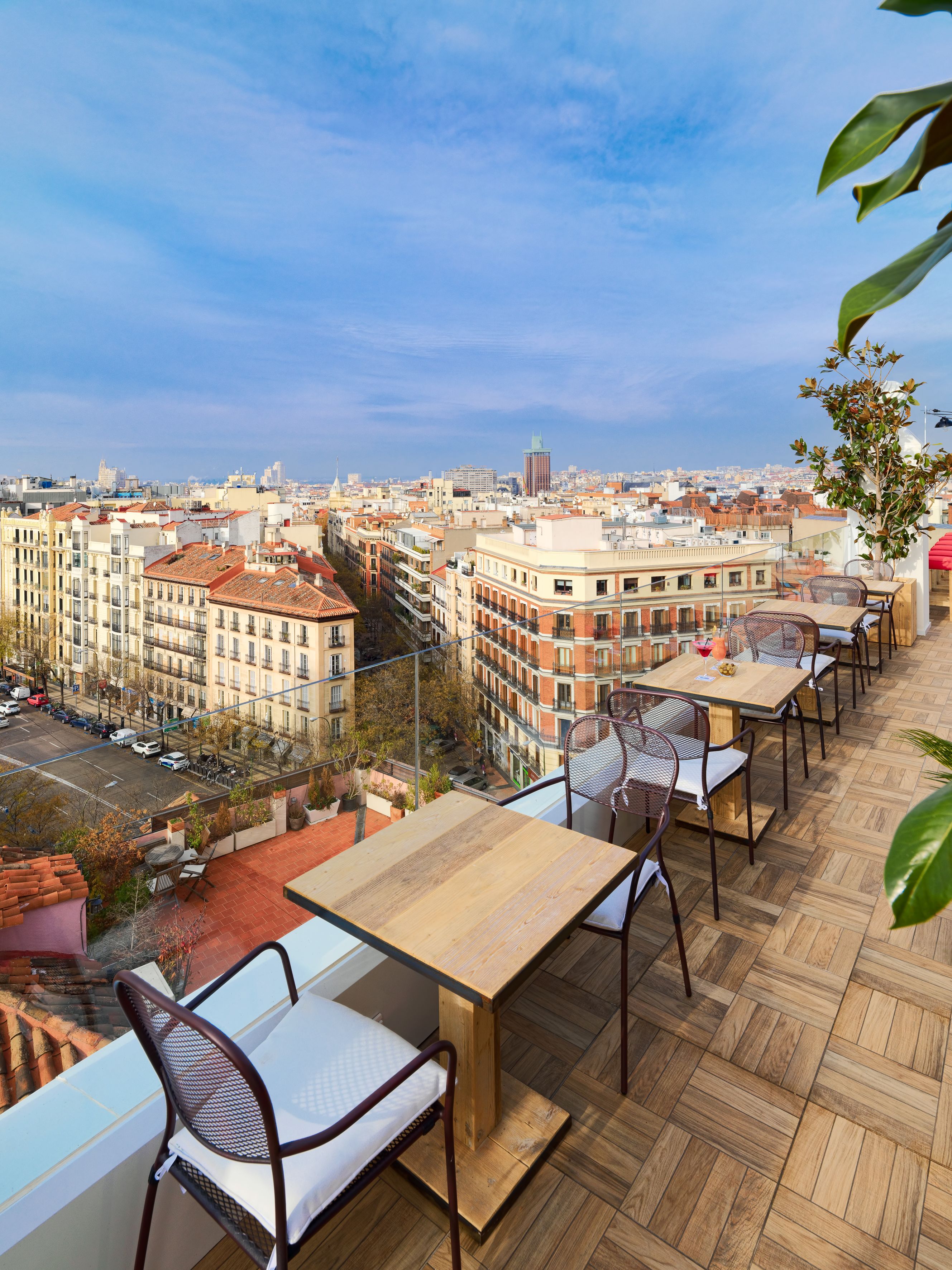 En tagterrasse med flere borde og stole, der giver et panoramaudsigt over byen.
