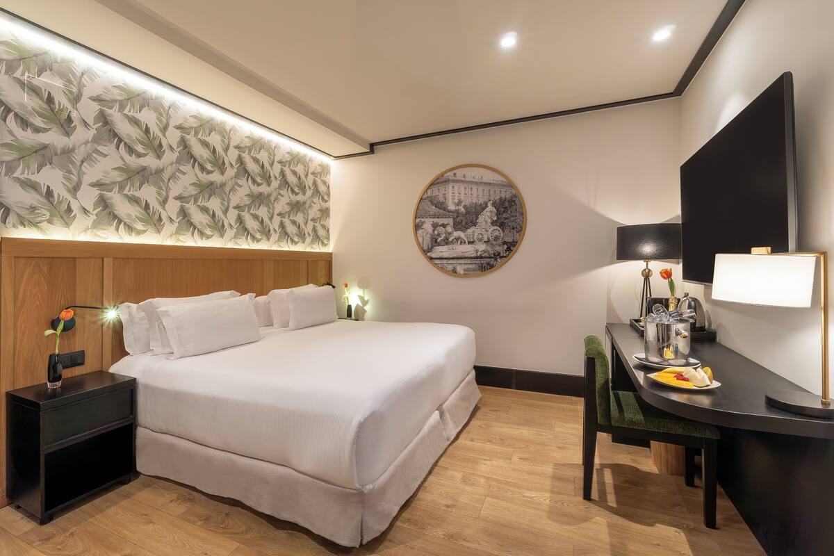 A neatly arranged hotel room with a large bed, a desk with a lamp, and a wall-mounted TV.
