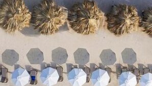 A beach with clear turquoise water and a sandy shore. There are several umbrella-like structures along the beach. - H10 Puerta de Alcalá 4* Sup (Madrid)
