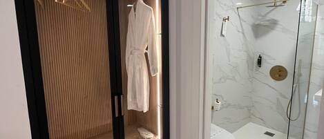 A modern bathroom with a glass-enclosed shower, a white toilet, and a wooden vanity with a robe hanging.