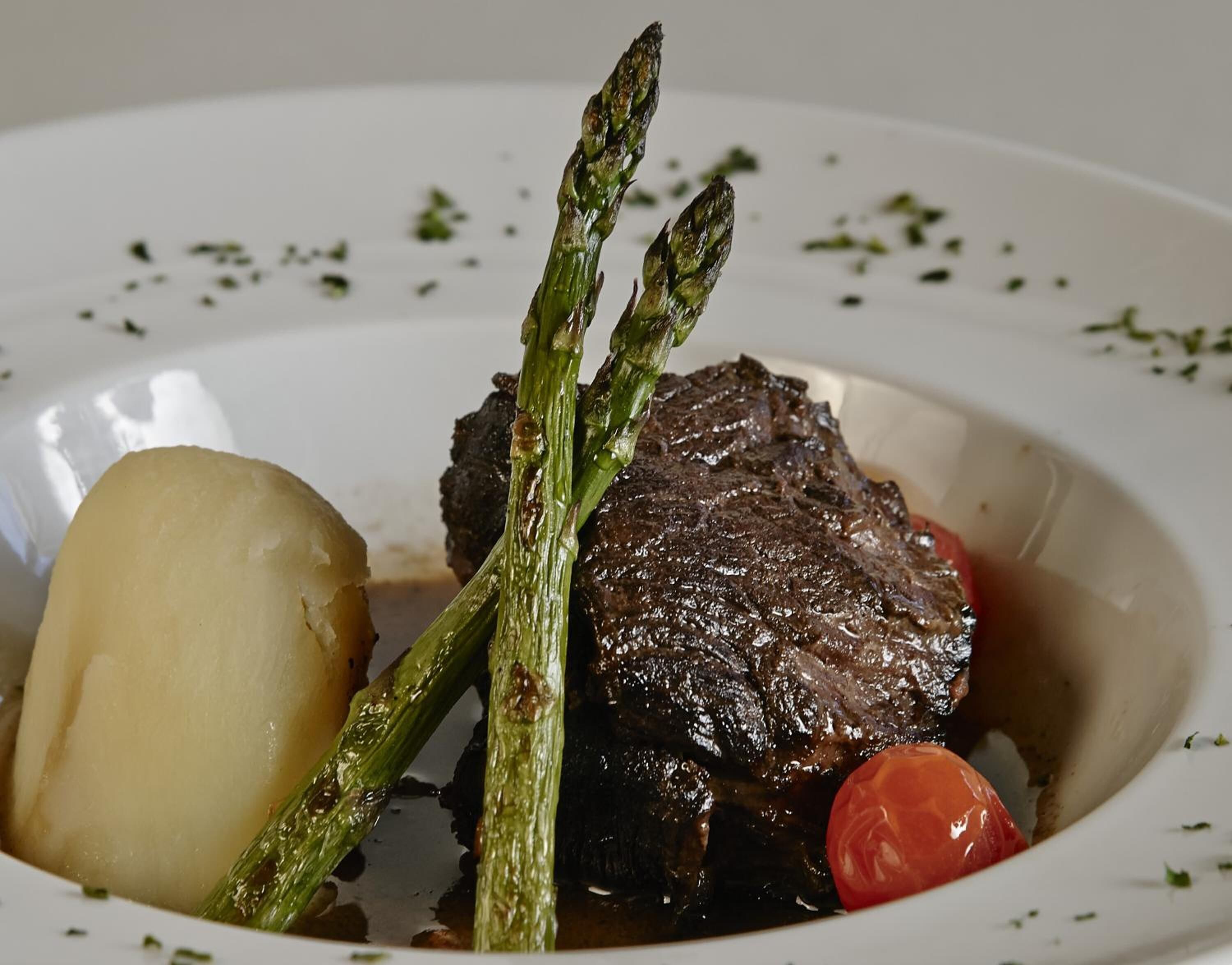 Ein Teller mit einem Steak, Spargel, einer Kartoffel und einer Kirschtomate.