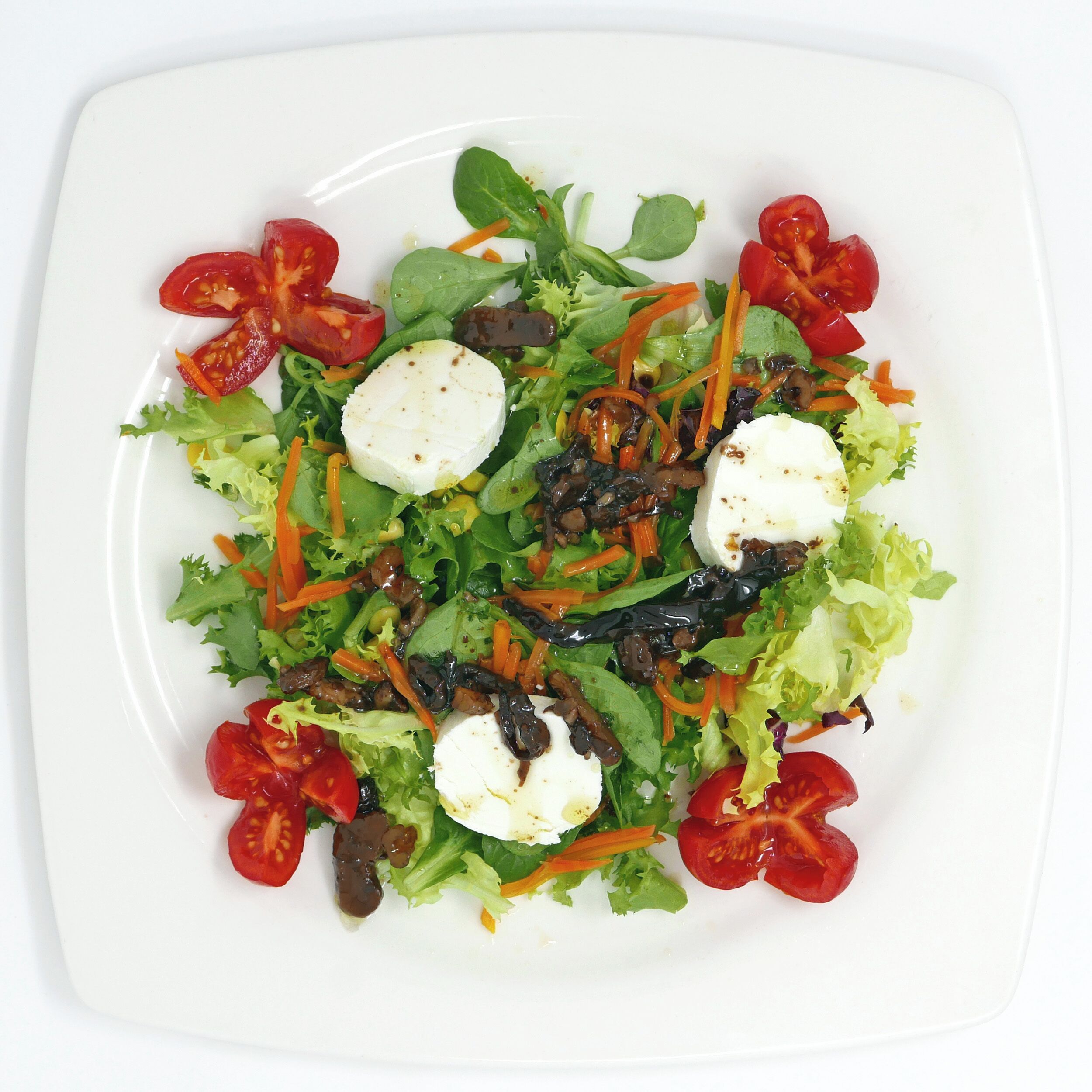Un plato blanco con una ensalada de lechuga, tomates cherry, zanahorias y queso.