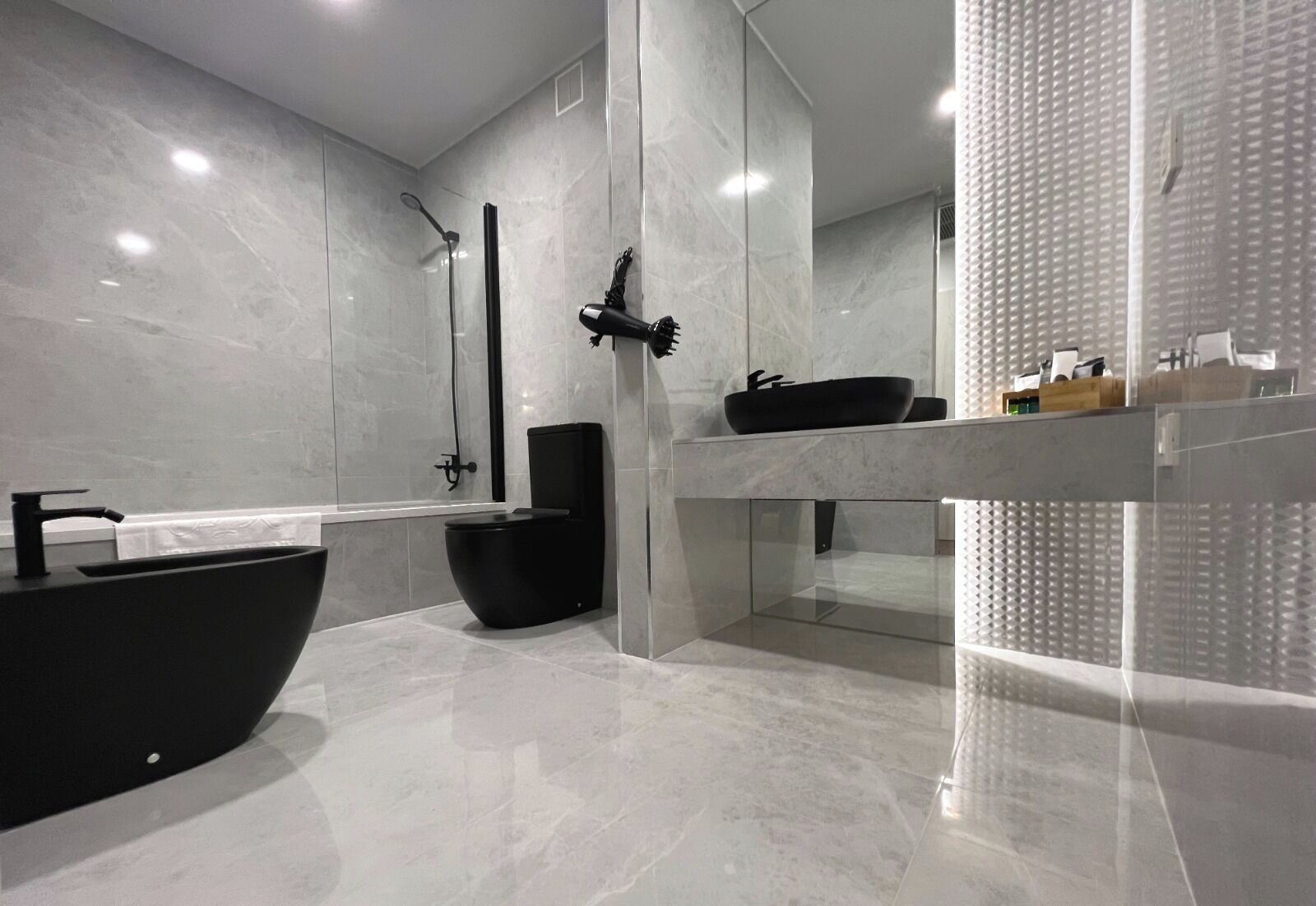 Un baño moderno con un lavamanos negro de diseño, un inodoro negro y una zona de ducha con mampara de vidrio.