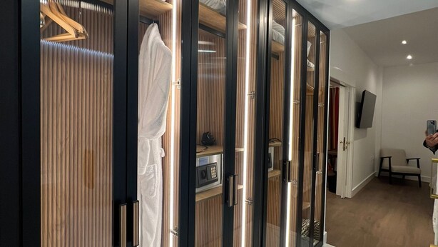 Una habitación de hotel moderna con vestidor que incluye puertas espejadas, paneles de madera y estantes integrados.