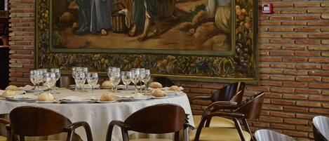 Un comedor con mesas dispuestas para una comida, un mural grande en la pared y paredes de ladrillo.