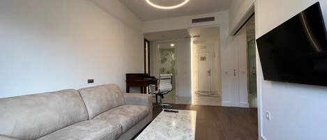 A modern living room with a sofa, a coffee table, a piano, and a TV mounted on the wall.