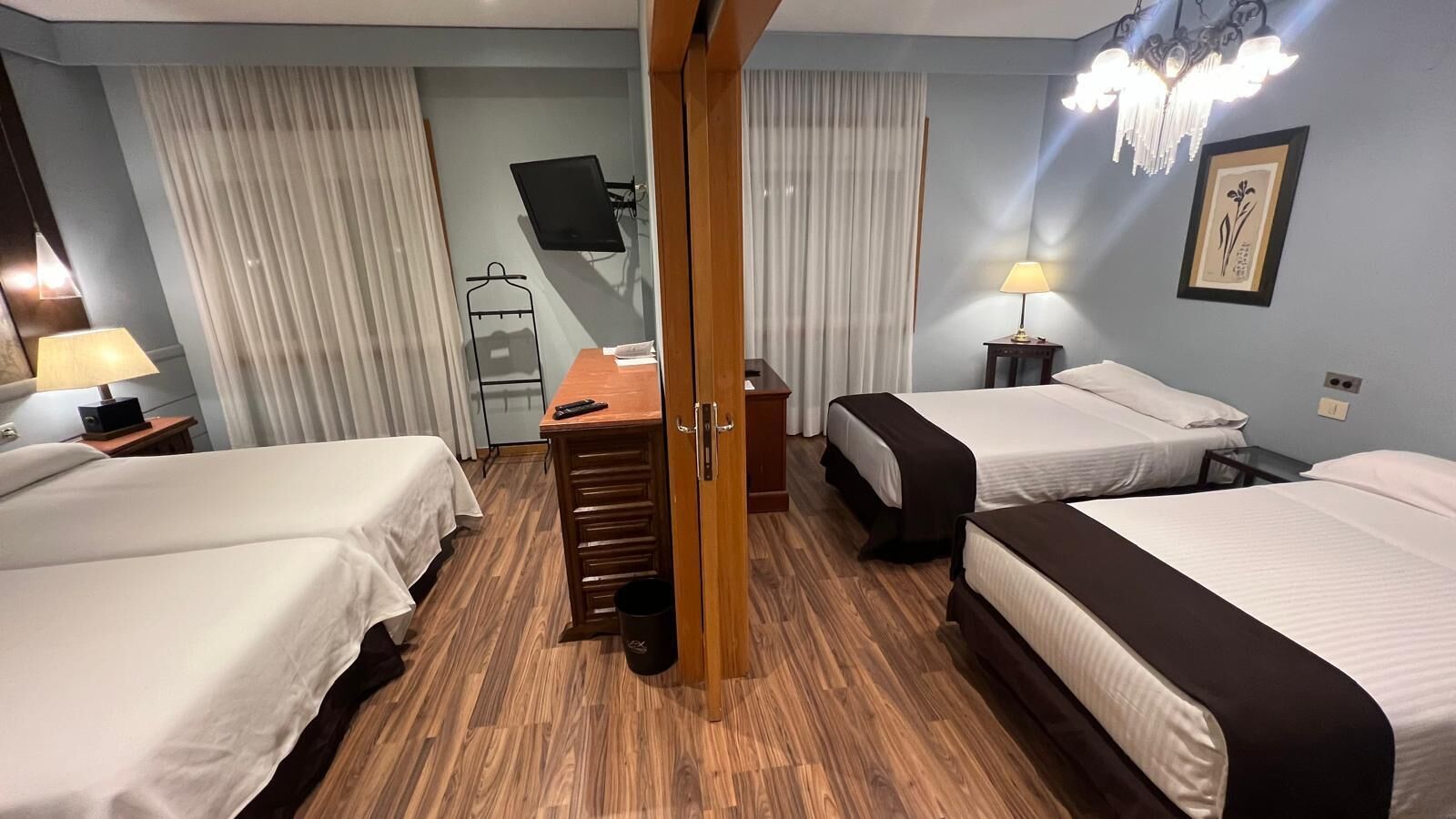 Habitació d'hotel amb dos llits, una taula de treball, una cadira, un televisor i un penjador de cristall.