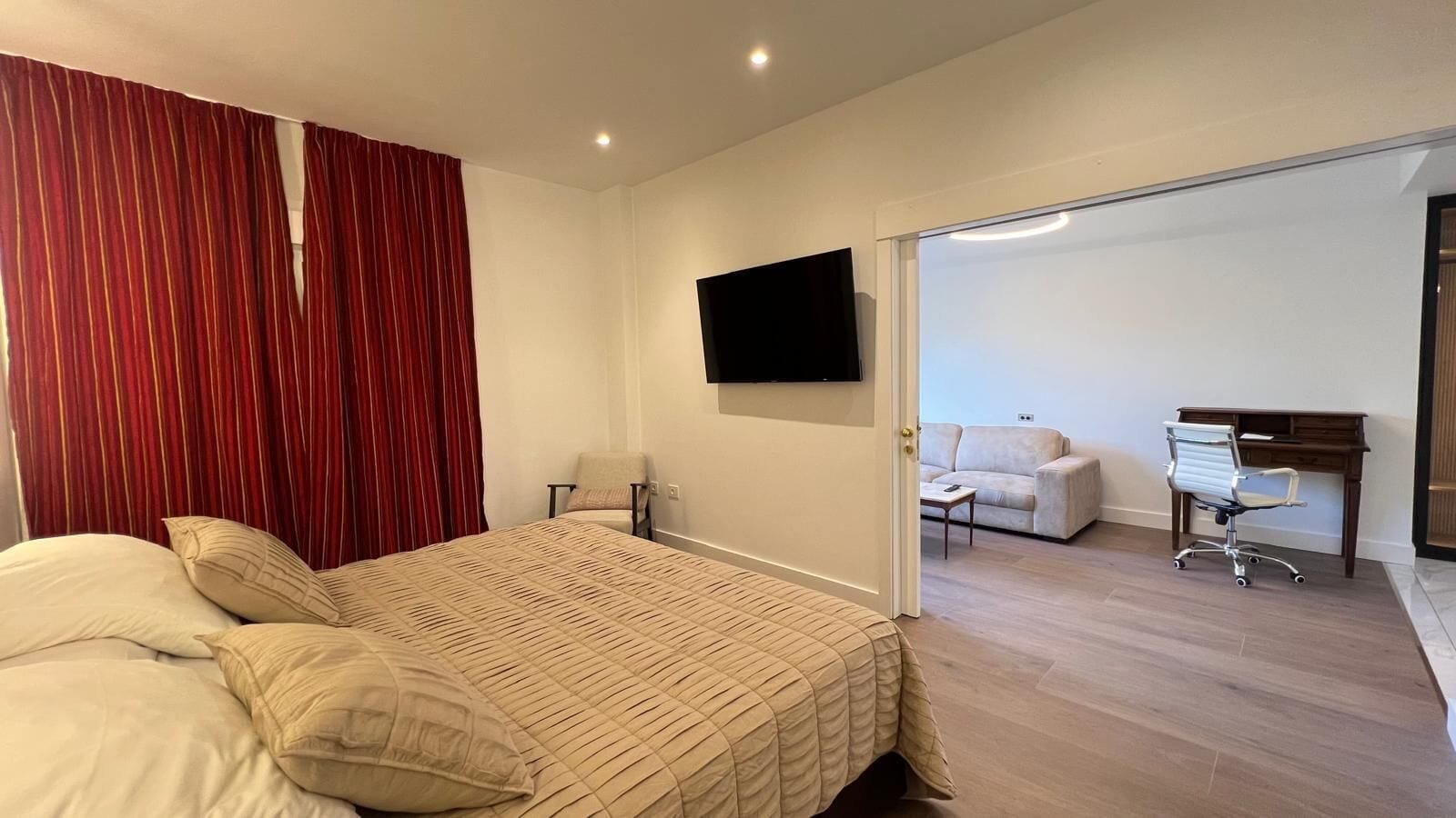 A hotel room with a bed, a desk, a chair, a TV, and a sofa.