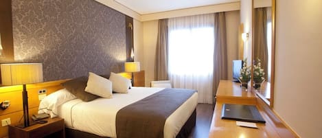 Hotelkamer met een groot bed, bedlampen, een bureau met een laptop, een spiegel en een raam met gordijnen.