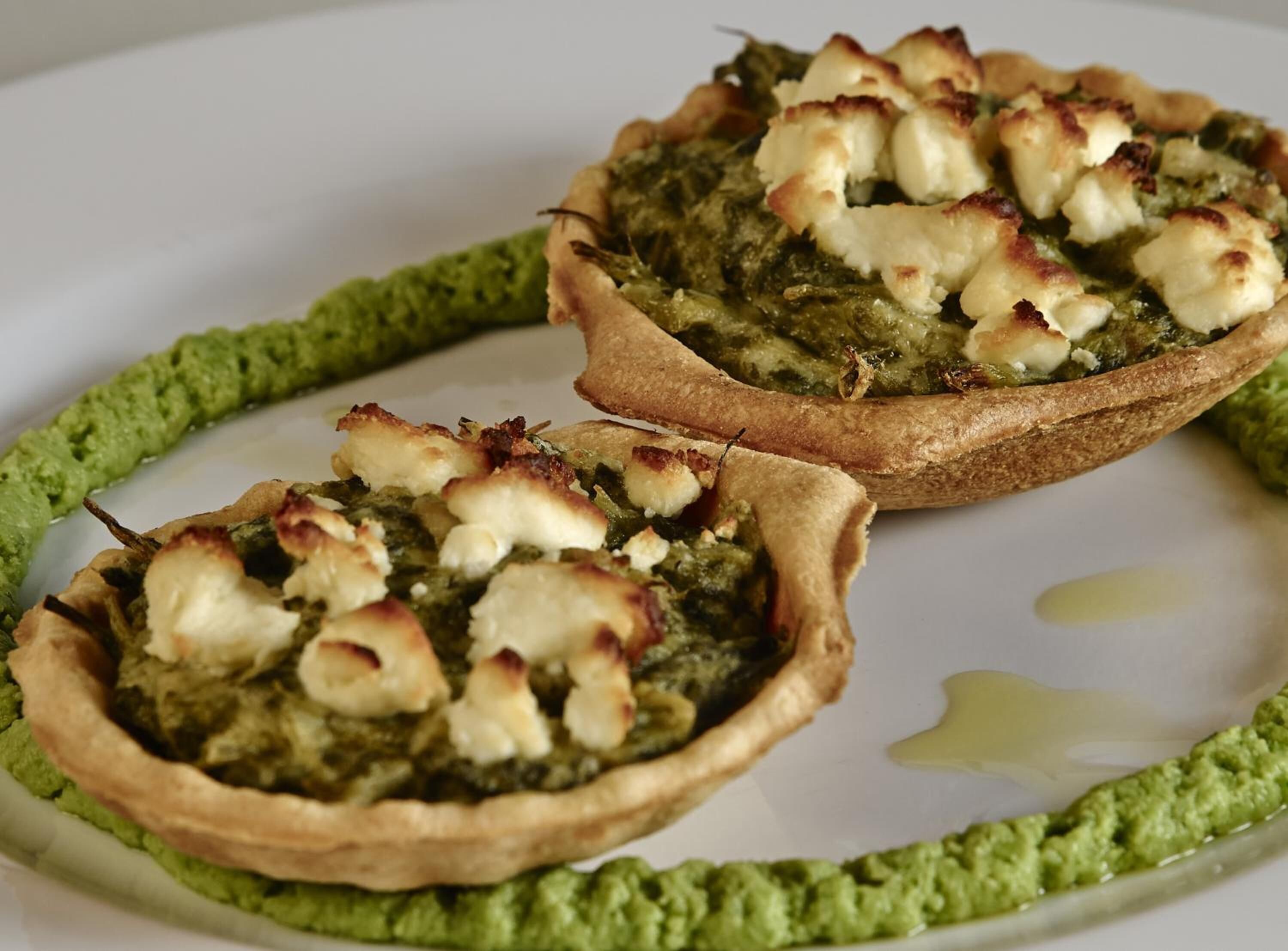 Dos empanadas sabrosas con relleno verde y queso sobre un plato blanco.