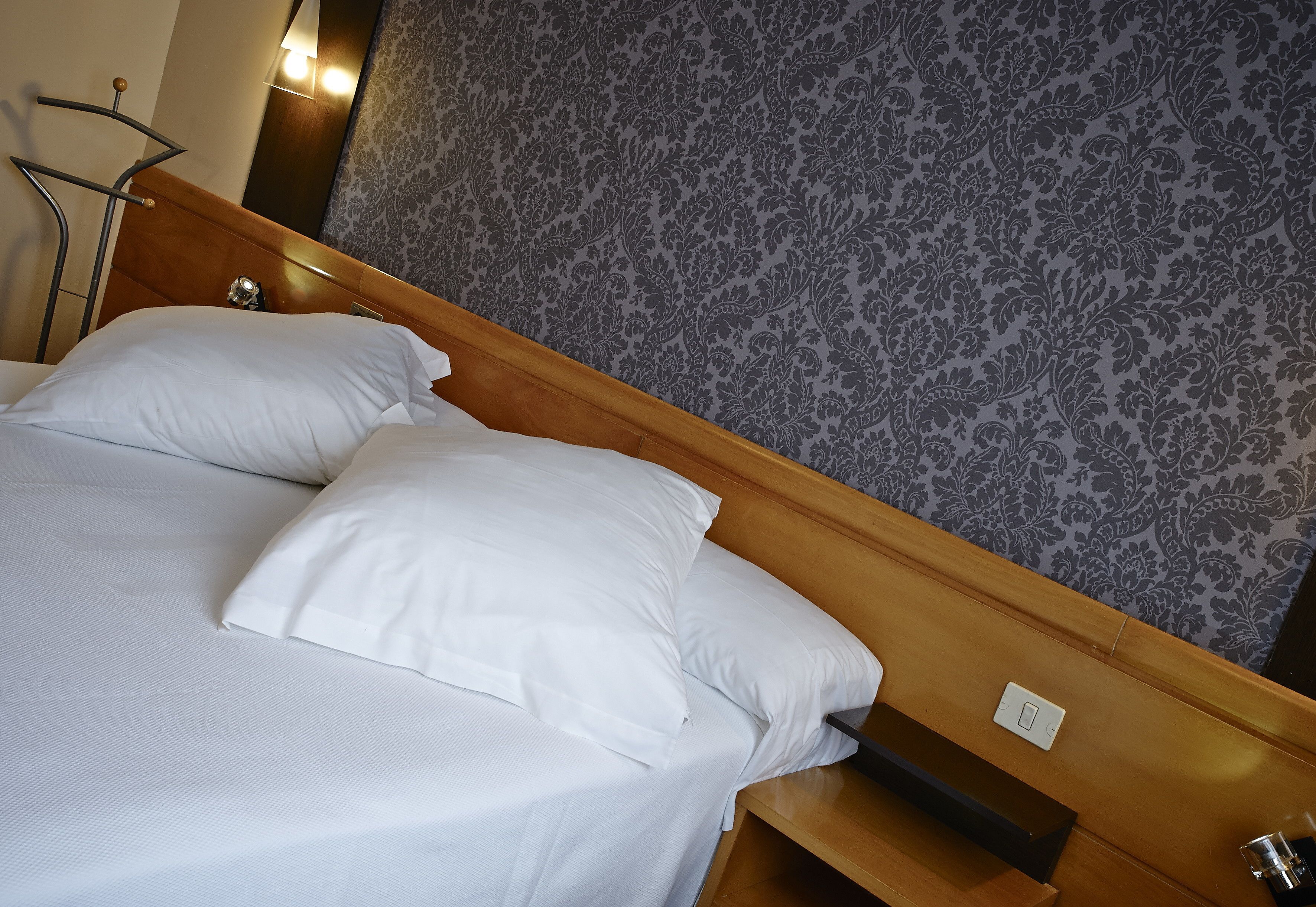 A neatly made bed with white linens and a wooden headboard.