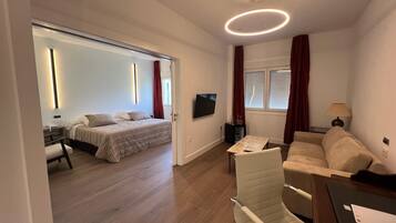 A modern hotel room with a bed, a sofa, a TV, and a desk.