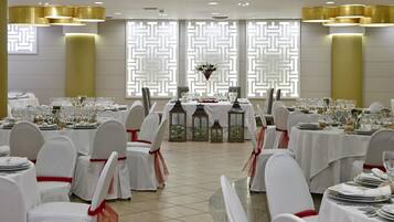 A banquet hall with round tables set for dining, white chairs with red sashes, and decorative lanterns.