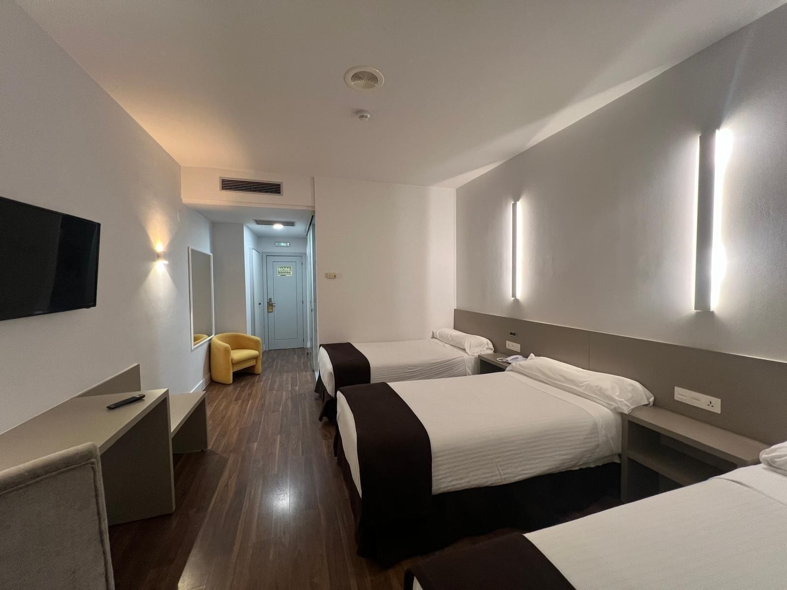 A hotel room with two beds, a desk, a chair, and a TV.