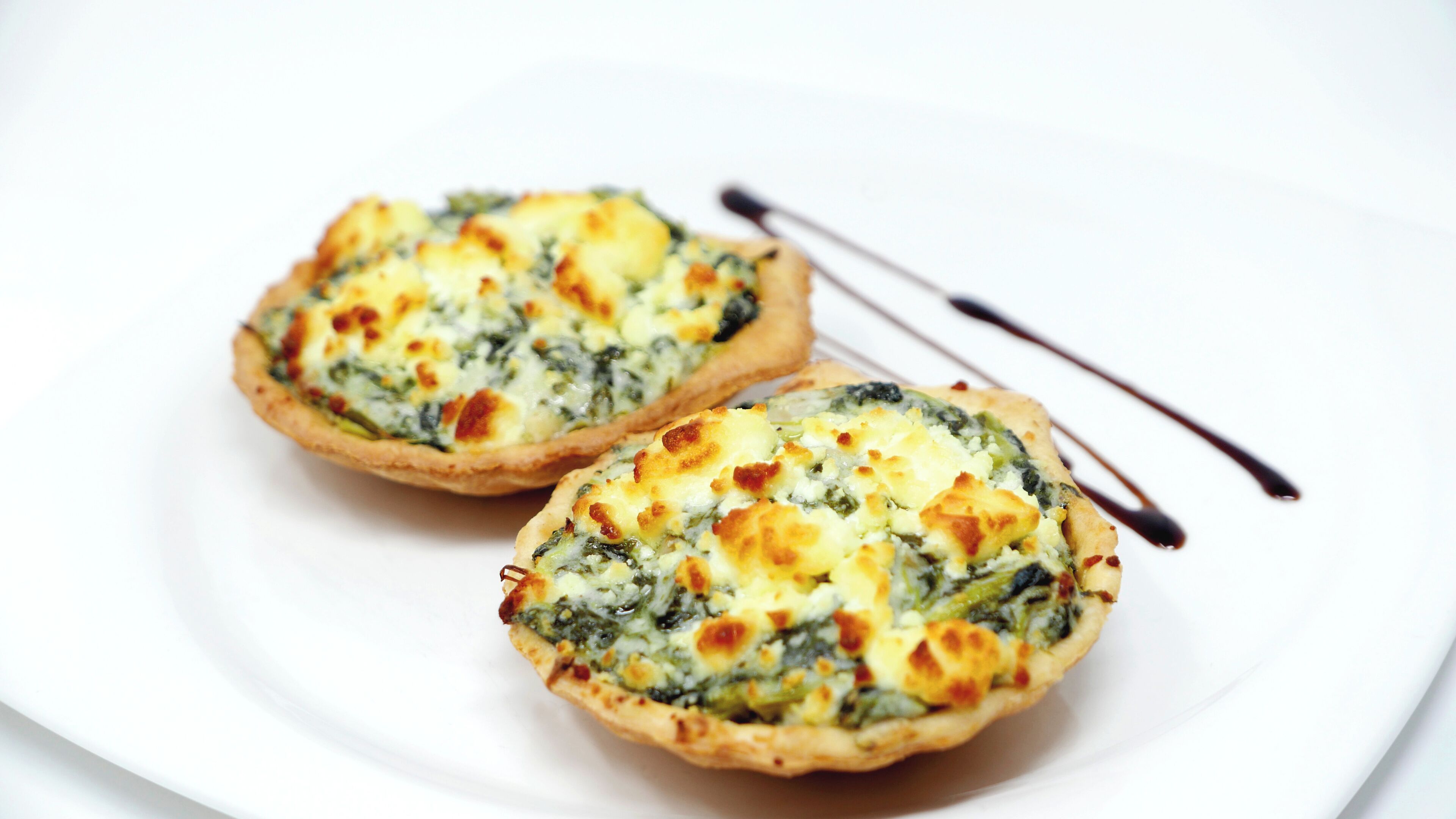 Two quiches on a white plate with a fork and knife.