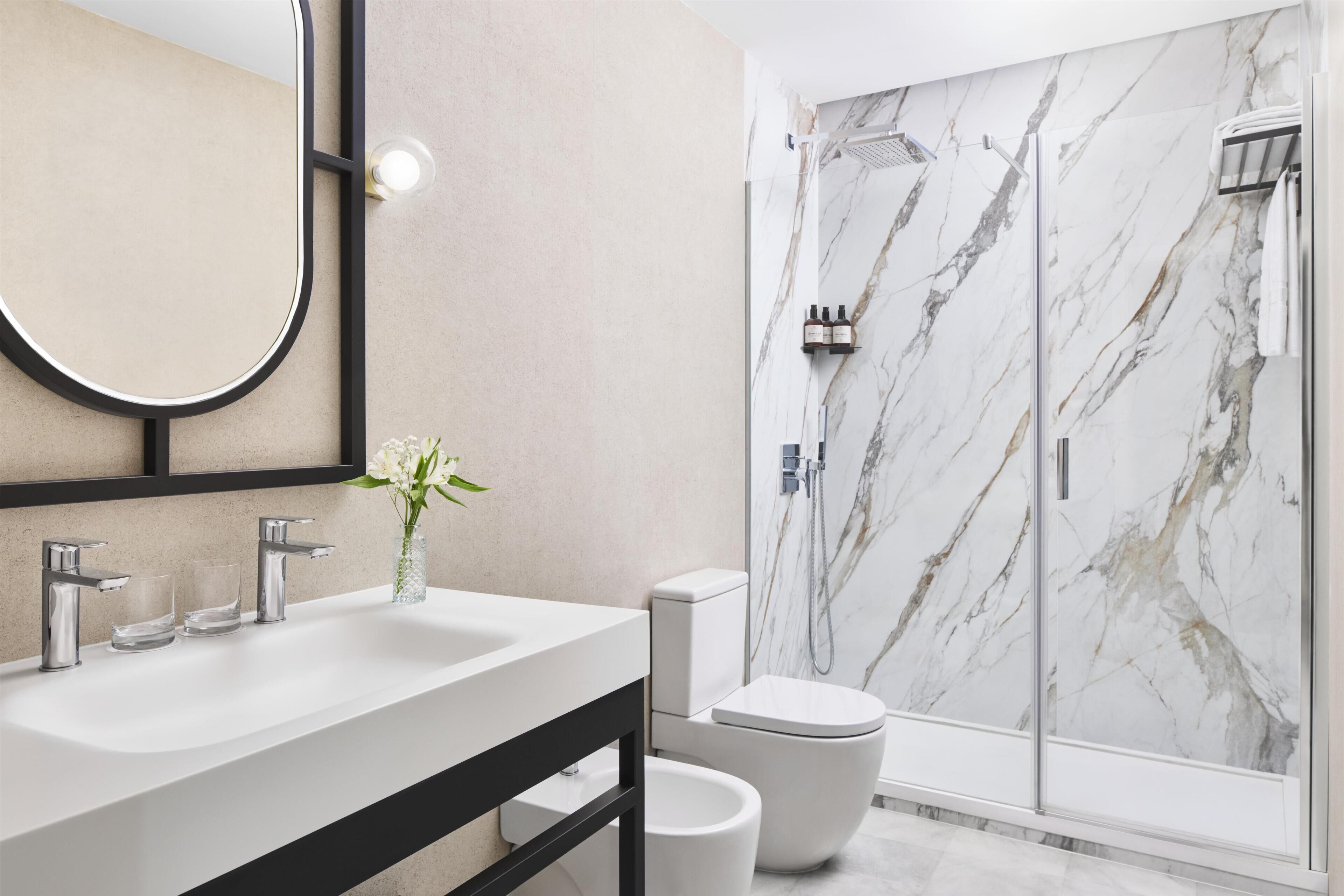 A modern bathroom with a marble shower wall, a large mirror, and a white sink.