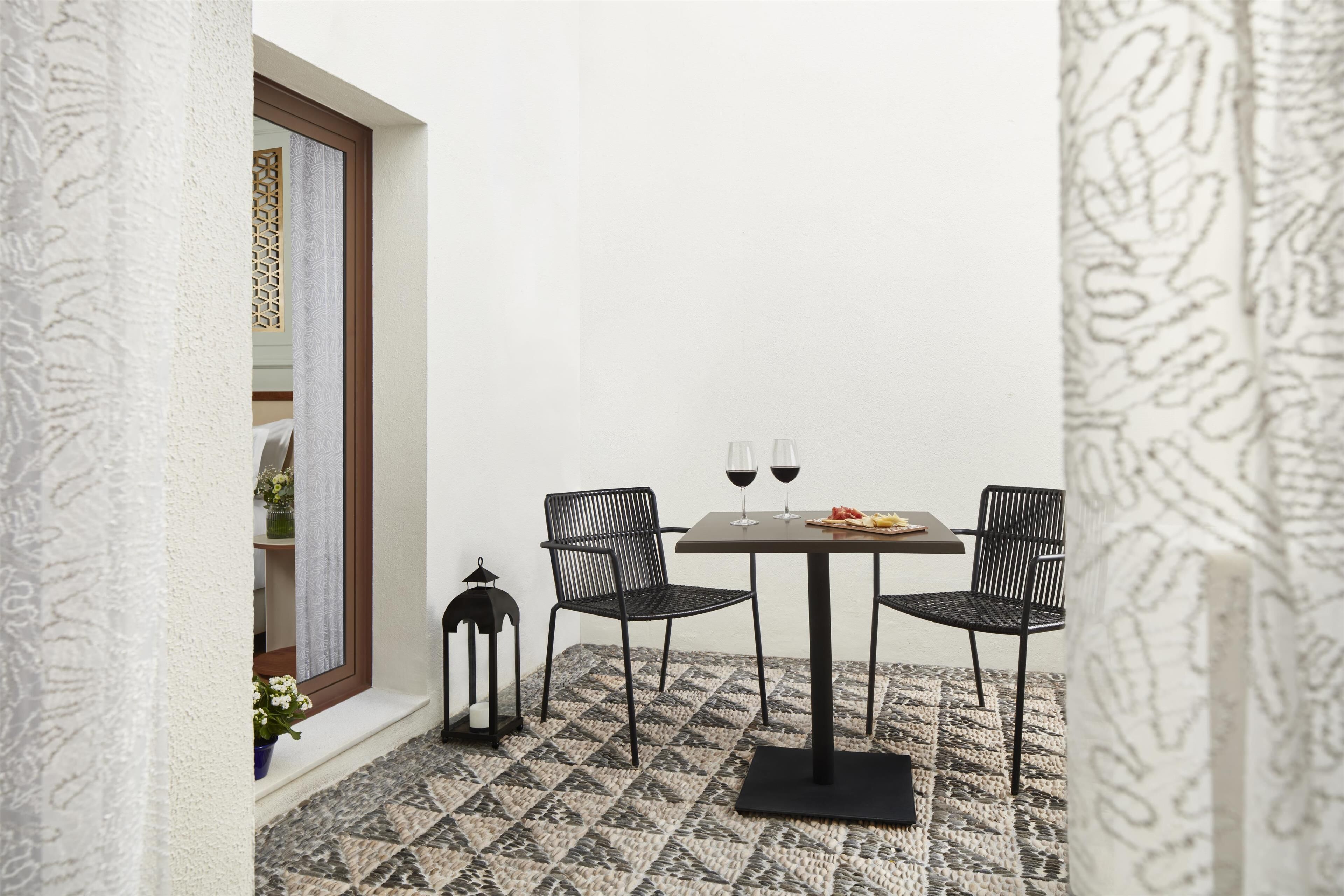 A small outdoor dining area with a table and four chairs, a lantern, and a window with a decorative screen.