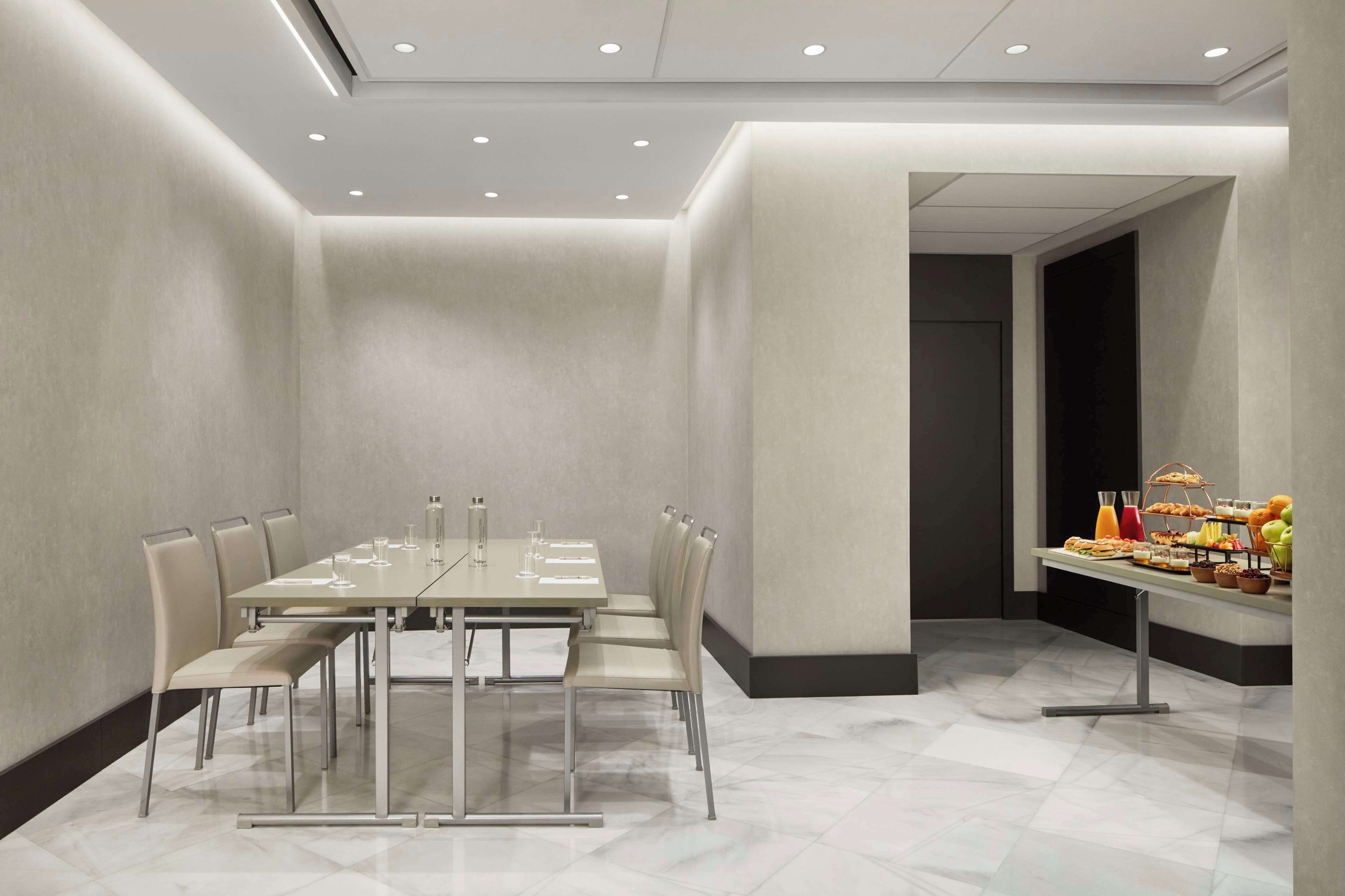 Un salón de conferencias con una mesa rectangular, seis sillas y una mesa de buffet con comida y bebidas.