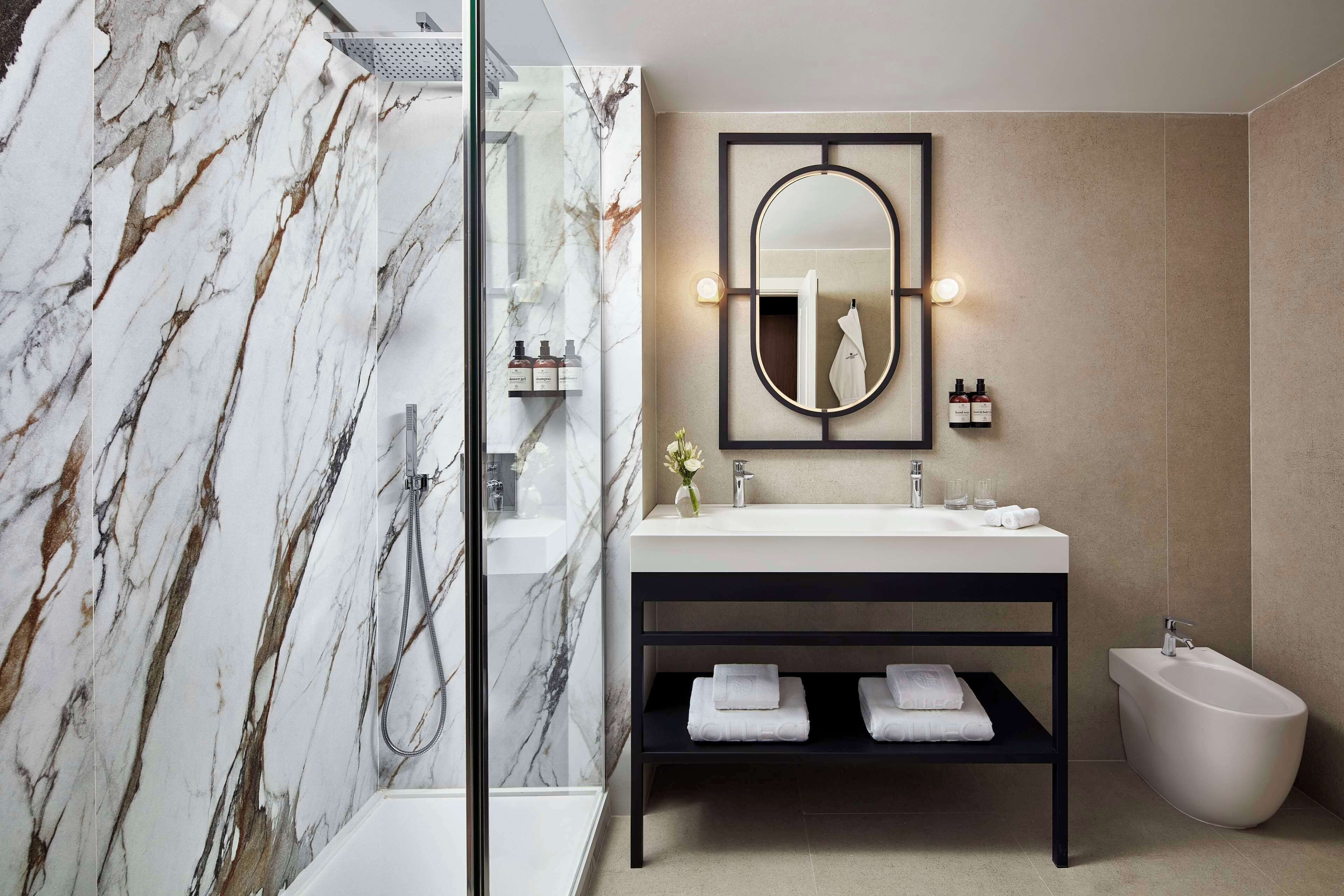 Un baño moderno con ducha de mármol, un espejo grande, un bidé y un tocador con toallas.