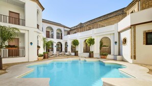 A swimming pool surrounded by white buildings with arches, potted plants, and outdoor seating. - NH Collection Palacio de Córdoba (Córdoba)