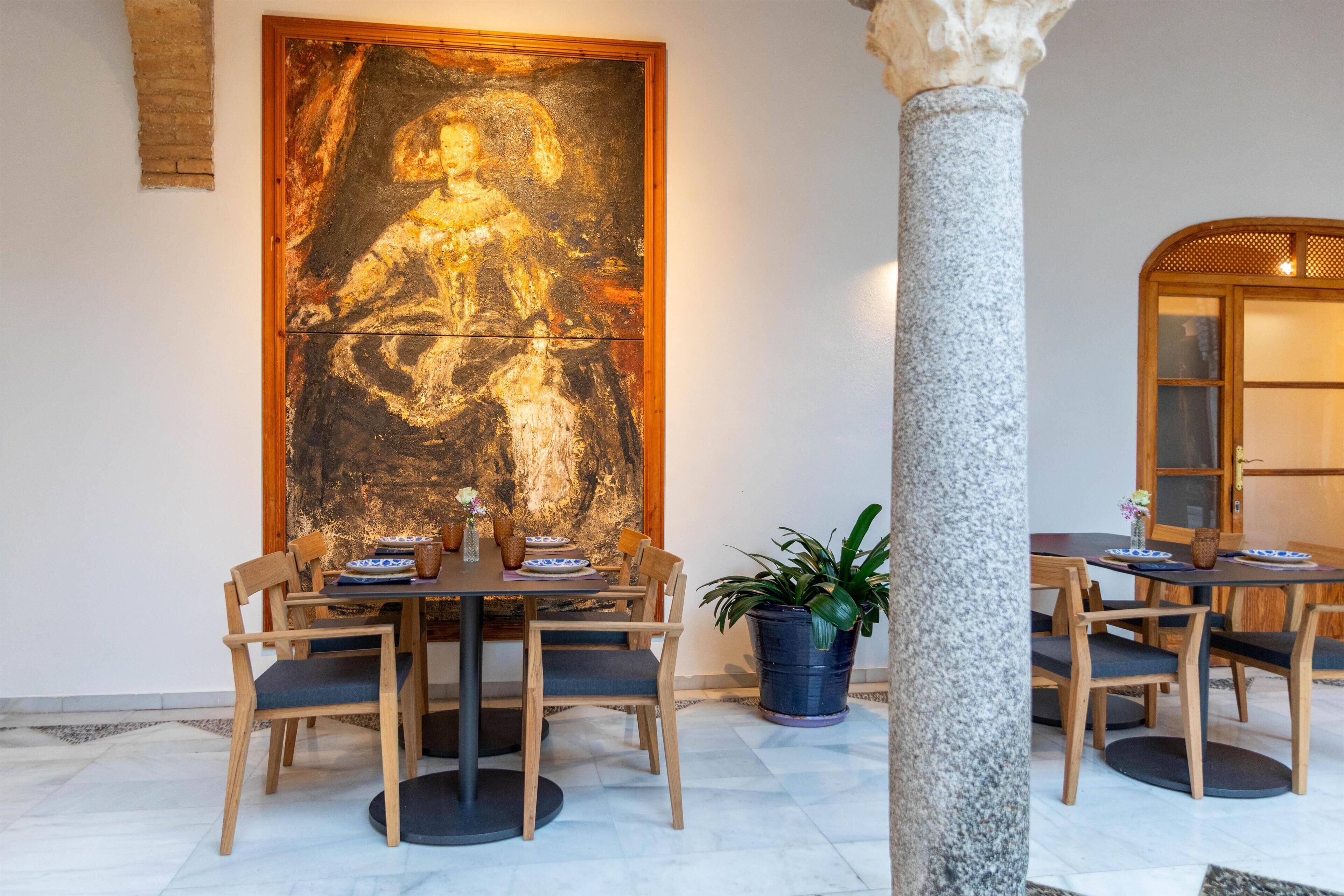 Un coin repas agrémenté d’un grand tableau, de chaises en bois, d’une table ronde et d’une plante en pot.