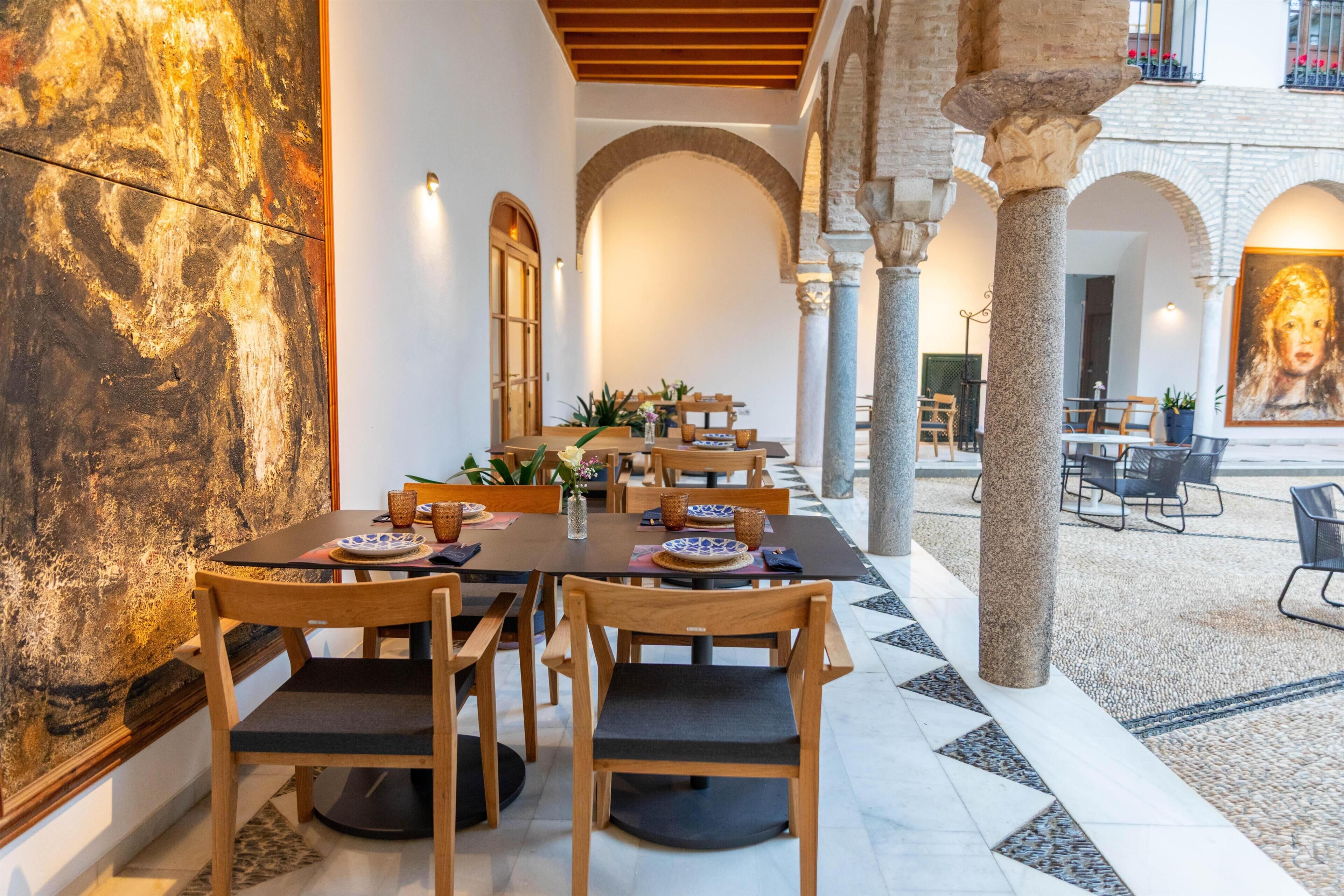 A dining area with wooden tables and chairs, a large abstract painting on the wall, and stone columns.