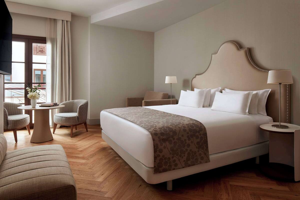 Una habitación de hotel con una cama grande, dos sillones, una mesita y una lámpara.