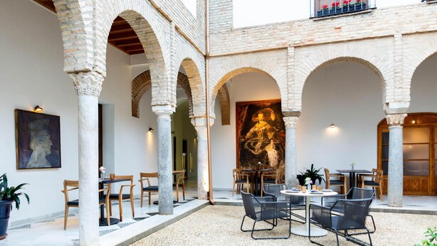 A courtyard with stone arches, outdoor seating, and a large mural. - NH Collection Palacio de Córdoba (Córdoba)