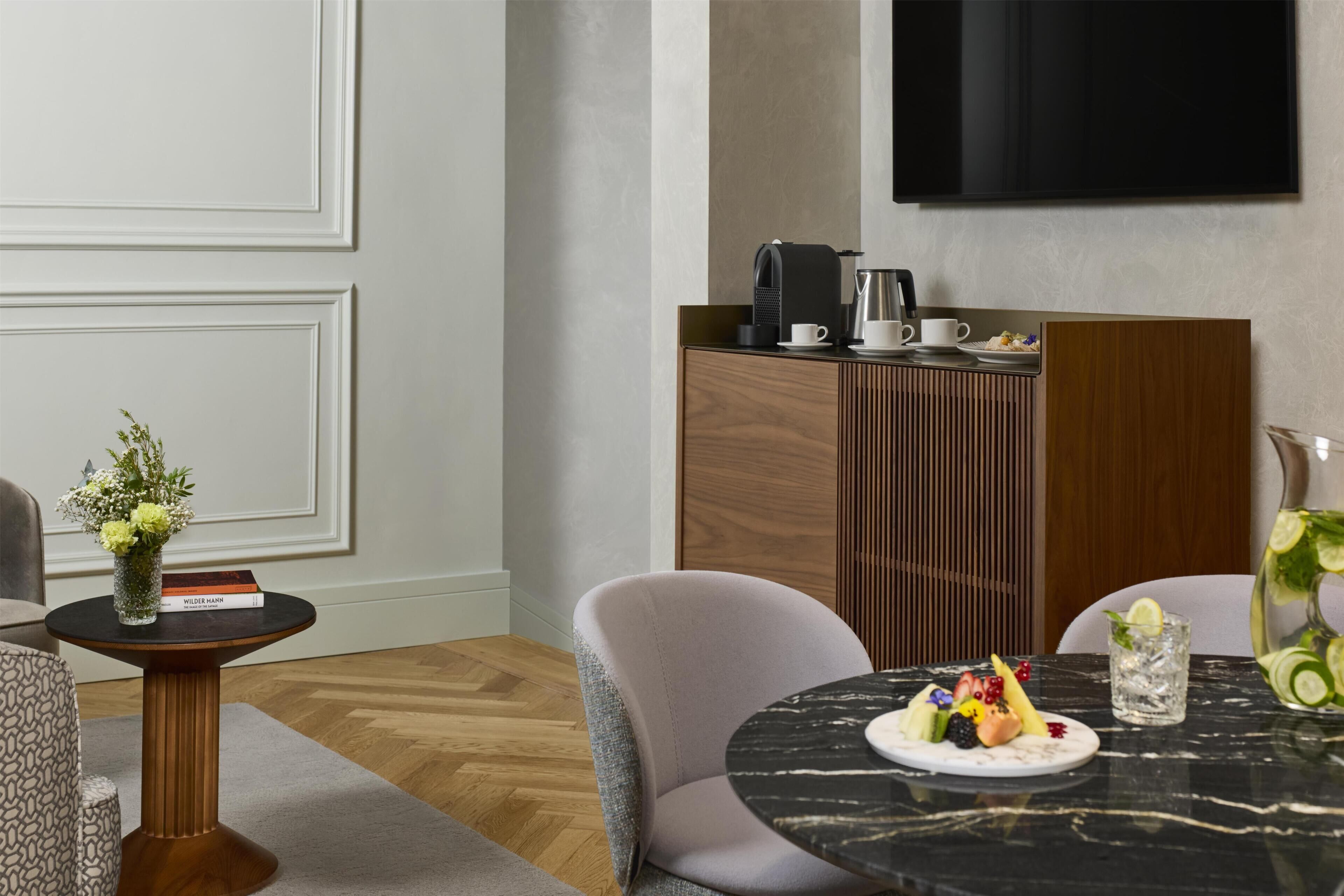 Ein modernes Hotelzimmer mit Essbereich, einer Kaffeestation und einem an der Wand befestigten Flachbildfernseher.