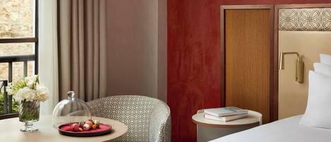 Una habitación de hotel con una cama, una mesa redonda con una bandeja de pasteles, una silla y un jarrón de flores.