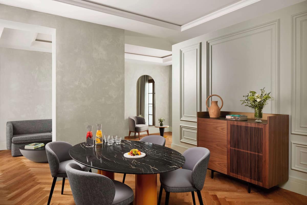 Un comedor moderno con una mesa redonda, sillas tapizadas en gris y un armario de madera con objetos decorativos.