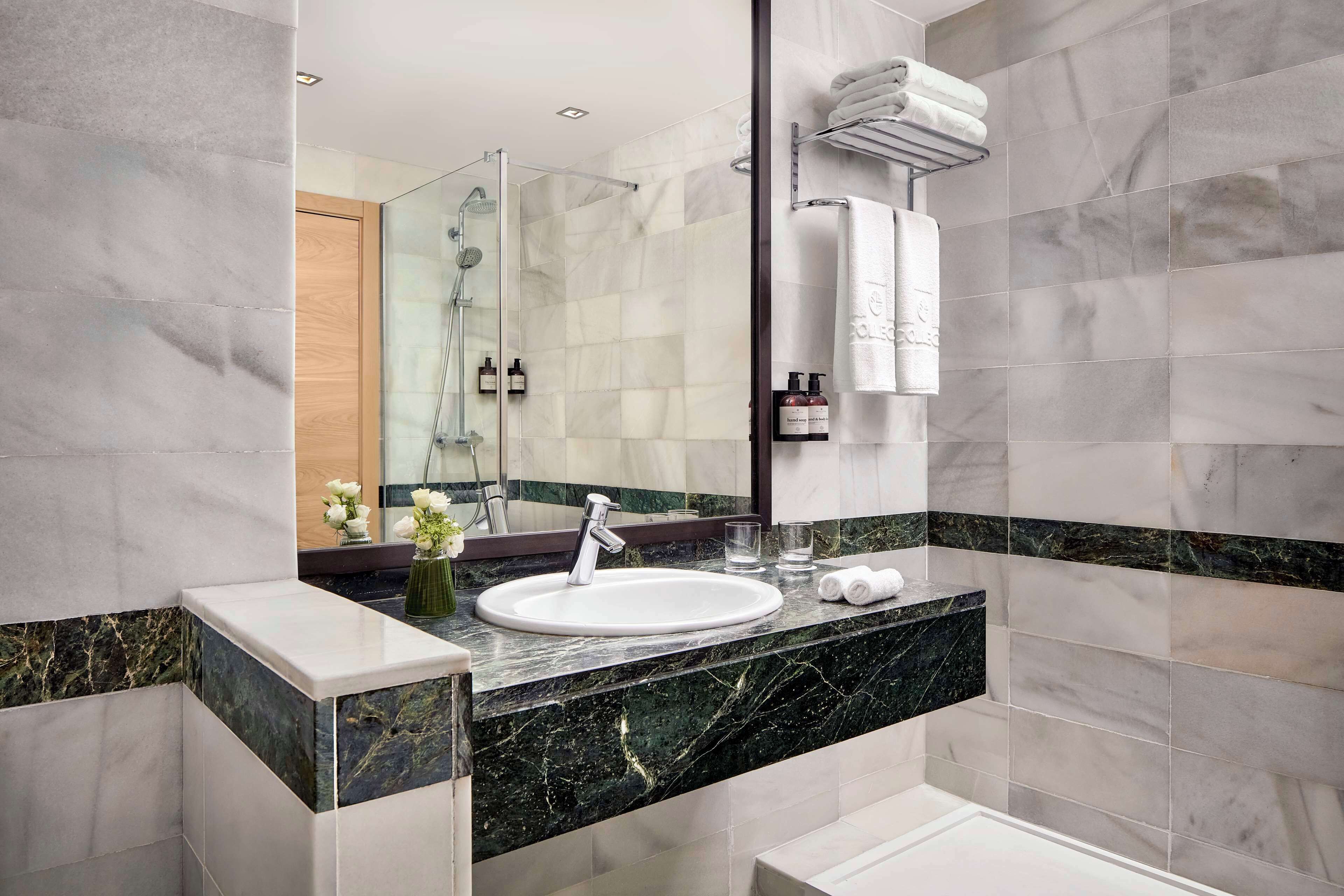 A modern bathroom with a marble sink, a large mirror, and a glass shower enclosure.