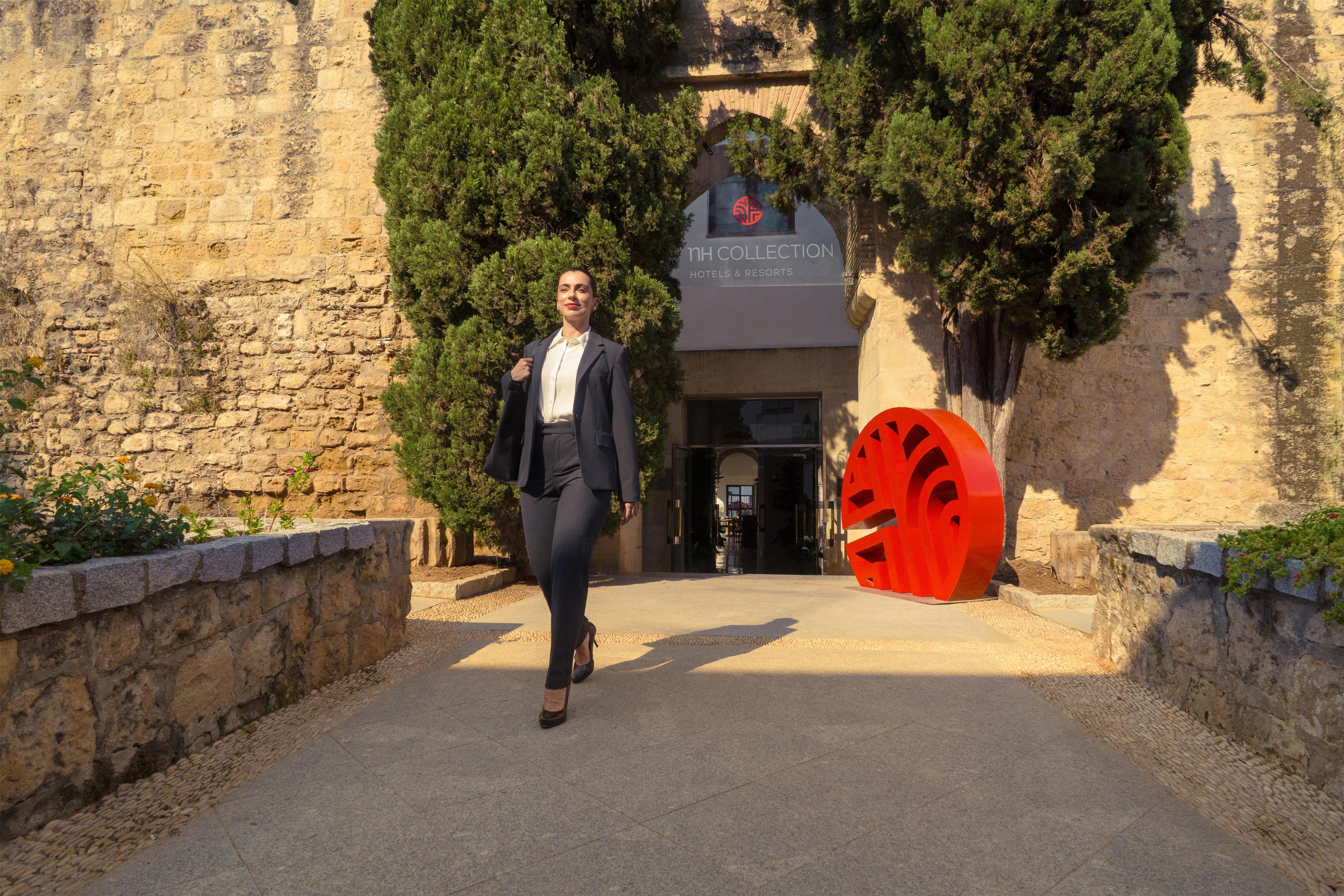 A person walking towards a building with a sign reading 'nh COLLECTION Hotels & Resorts'.
