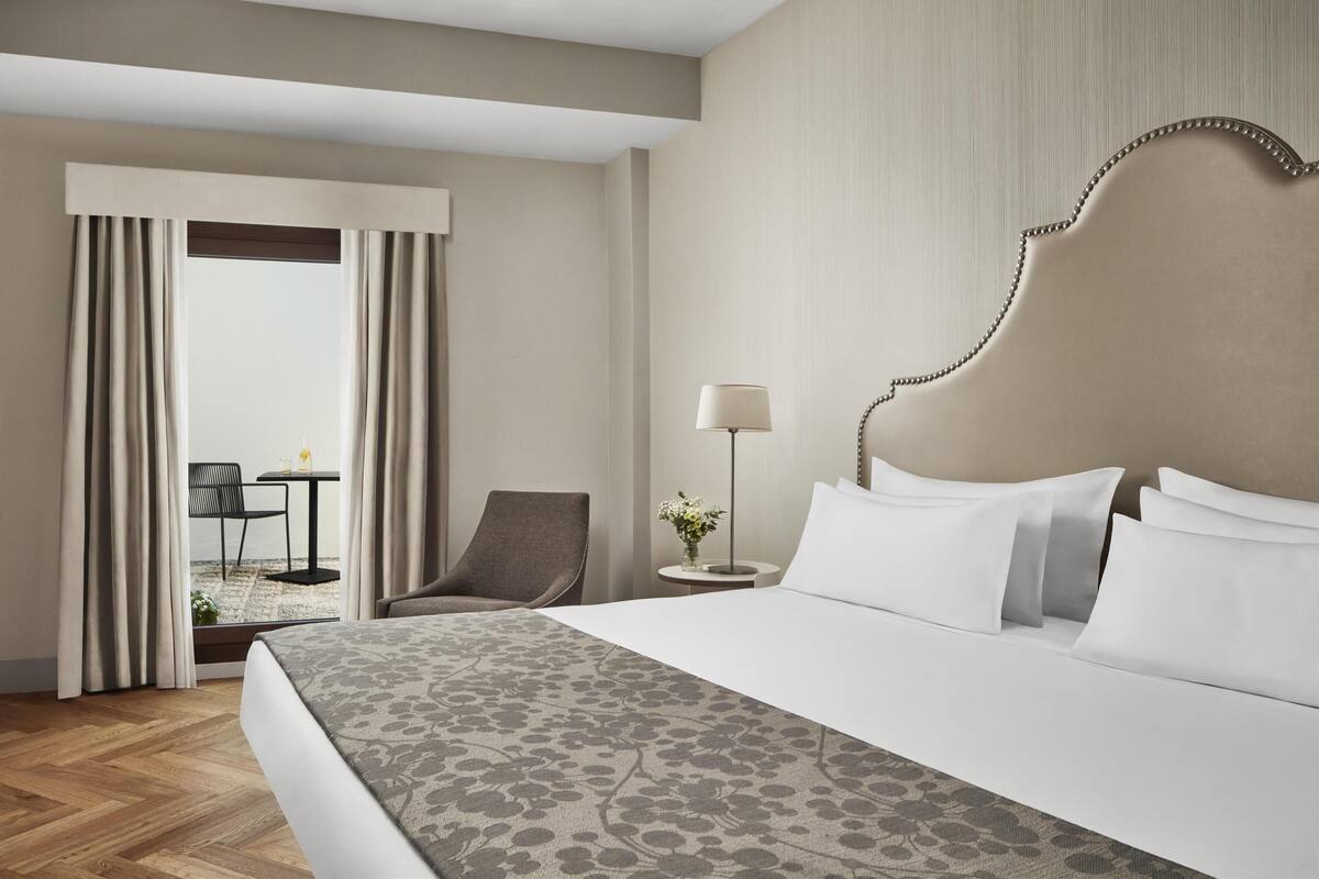 Una habitación de hotel con una cama grande, una silla, una mesita y una lámpara.