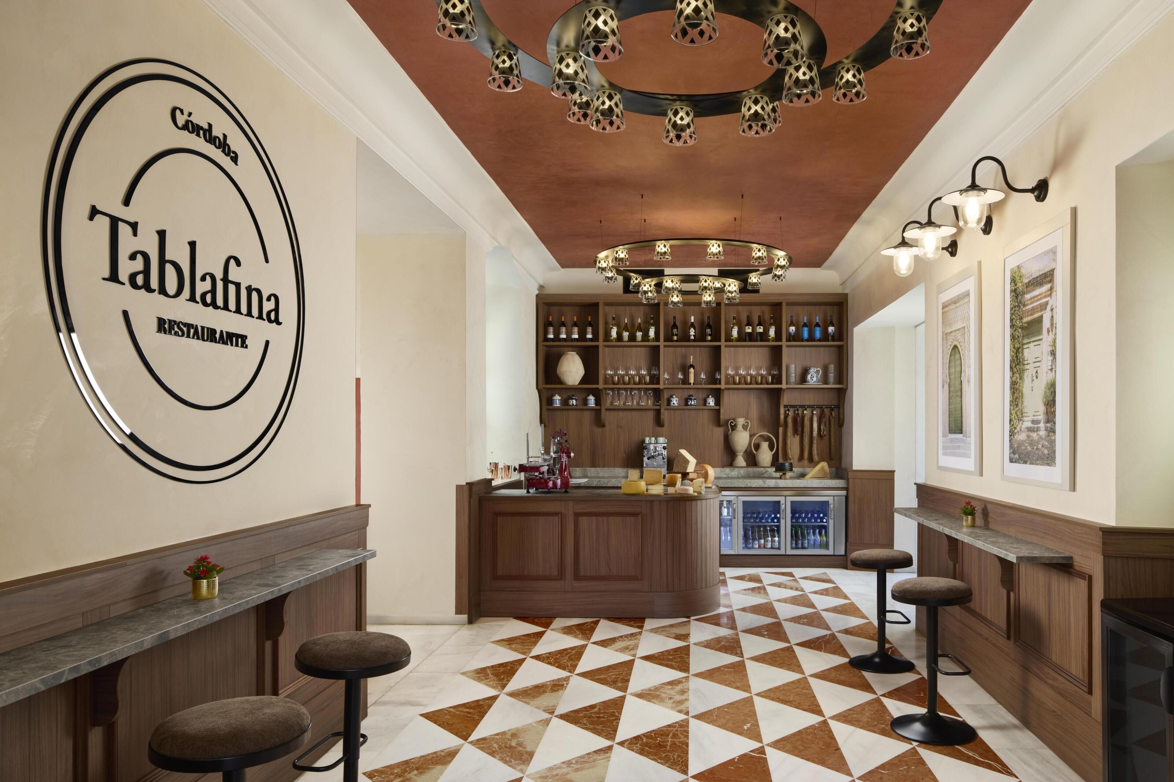 Un interior de restaurante con suelo de tablones, zona de bar de madera e isla central con taburetes.
