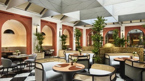 Un hall d’hôtel avec un sol à carreaux, des tables rondes entourées de chaises en osier et des plafonds en forme d’arc.