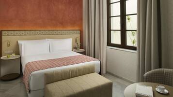 Habitación de hotel con cama, mesitas de noche, sofá, ventana con cortinas y vista a zonas verdes.