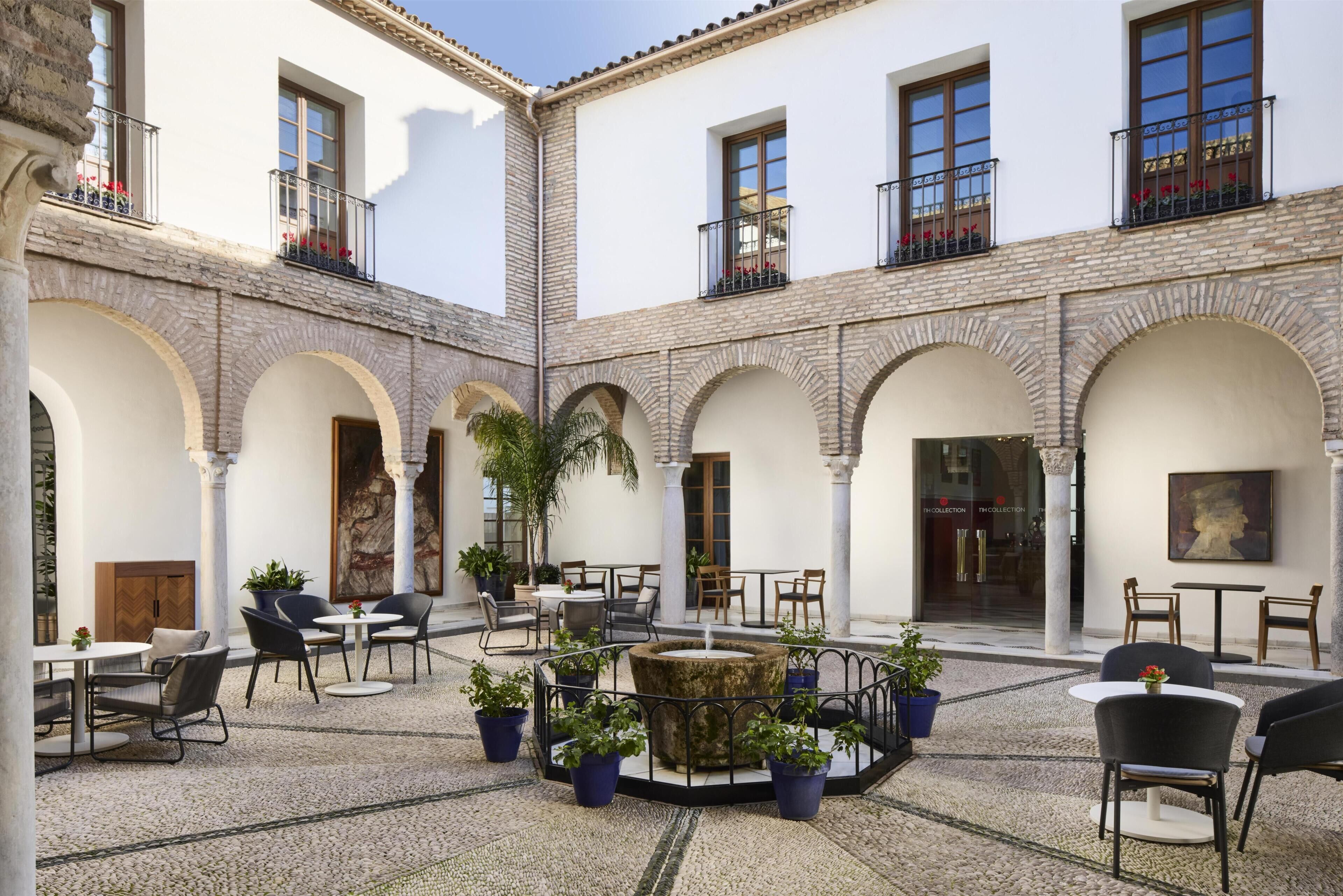 Un patio con mobiliario exterior, plantas en macetas y una fuente.