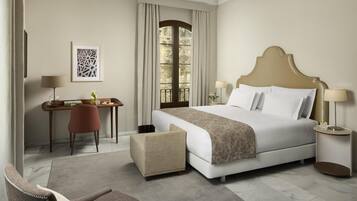 A hotel room with a bed, a desk, a chair, a window, and a lamp.