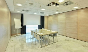 Un salón de conferencias con una gran mesa, sillas, una pizarra y una pantalla de proyector.