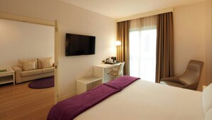 Habitación de hotel con cama, escritorio, silla, televisión y ventana con cortinas.