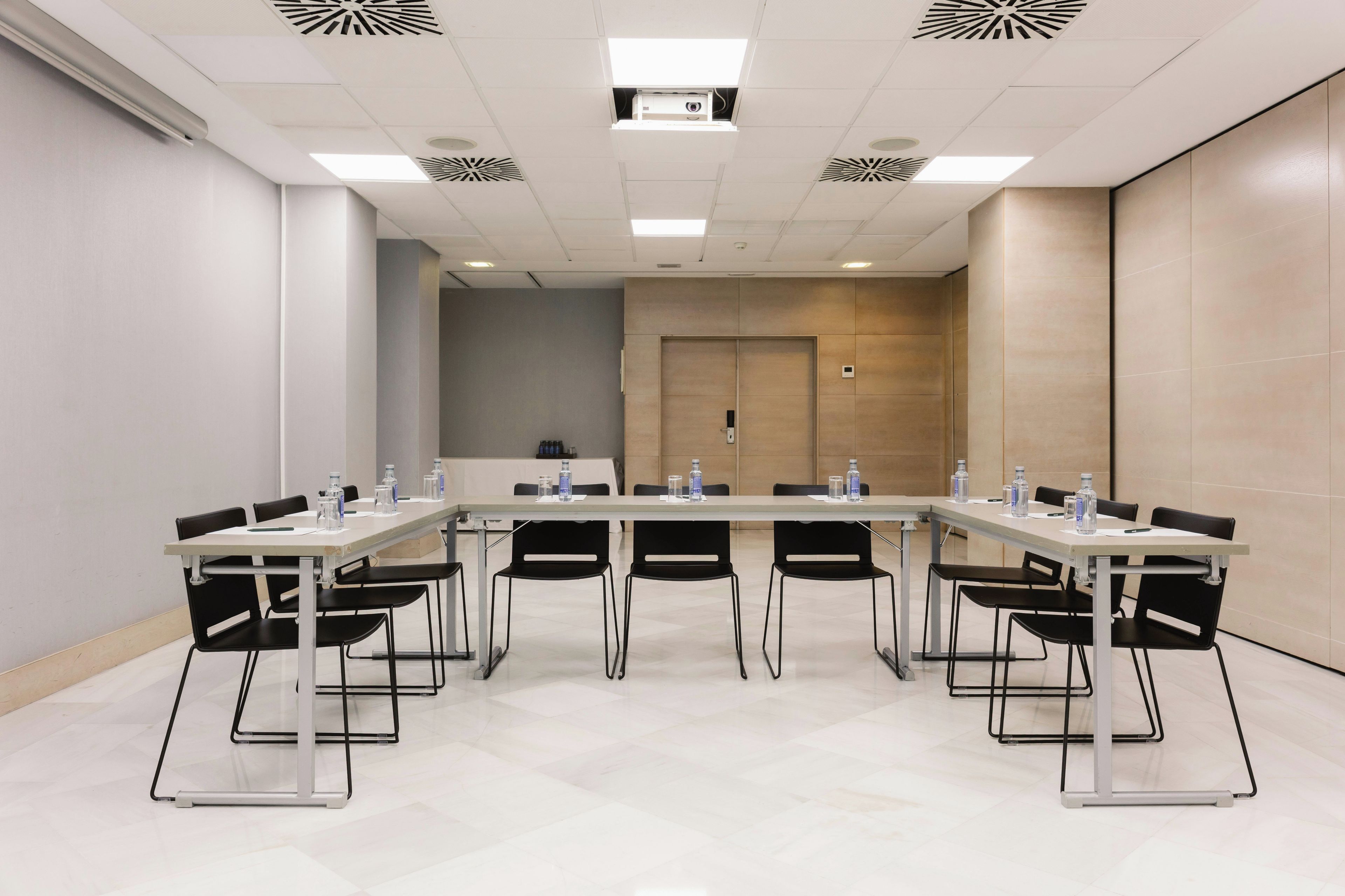 Un salón de conferencias con una larga mesa, sillas negras y botellas de agua.