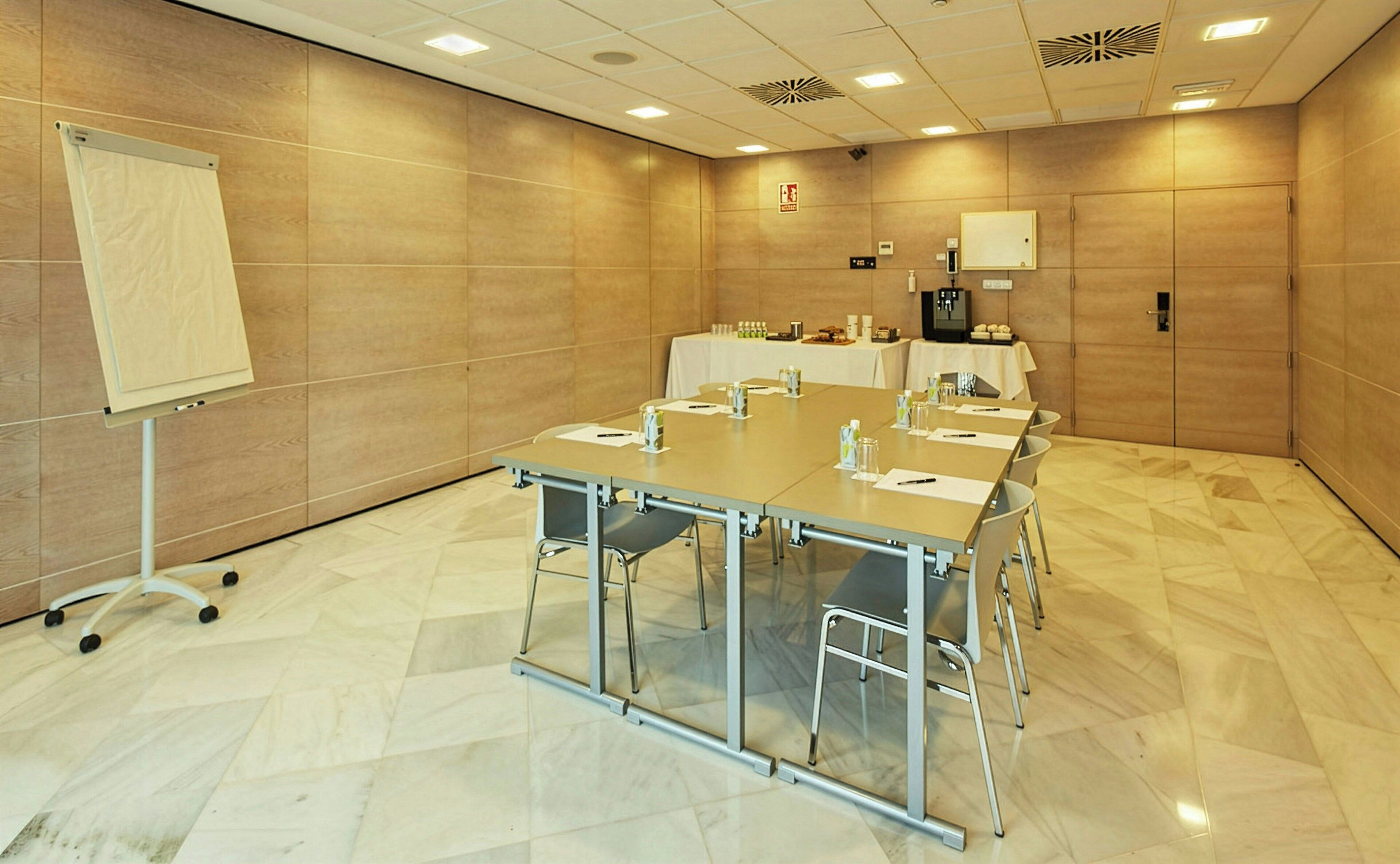 A conference room with a long table, chairs, a whiteboard, and a coffee machine.
