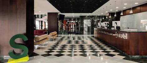 A hotel lobby with a checkered floor, a reception desk, and a large S-shaped letter decoration.